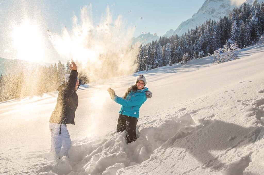 Zwei Personen werfen Schnee im verschneiten Hochgebirge und genießen den Winterspaß.