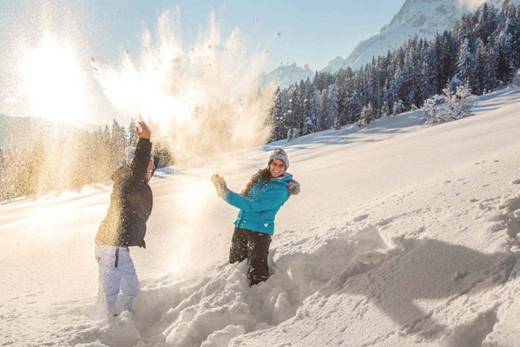 Zwei Personen im Schnee, lachen und werfen Schneeverwehungen in die Luft. Winterfreude am Hochkönig.