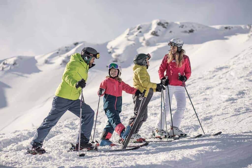 Familie beim Skifahren in den Bergen, umgeben von Schnee und atemberaubender Natur.