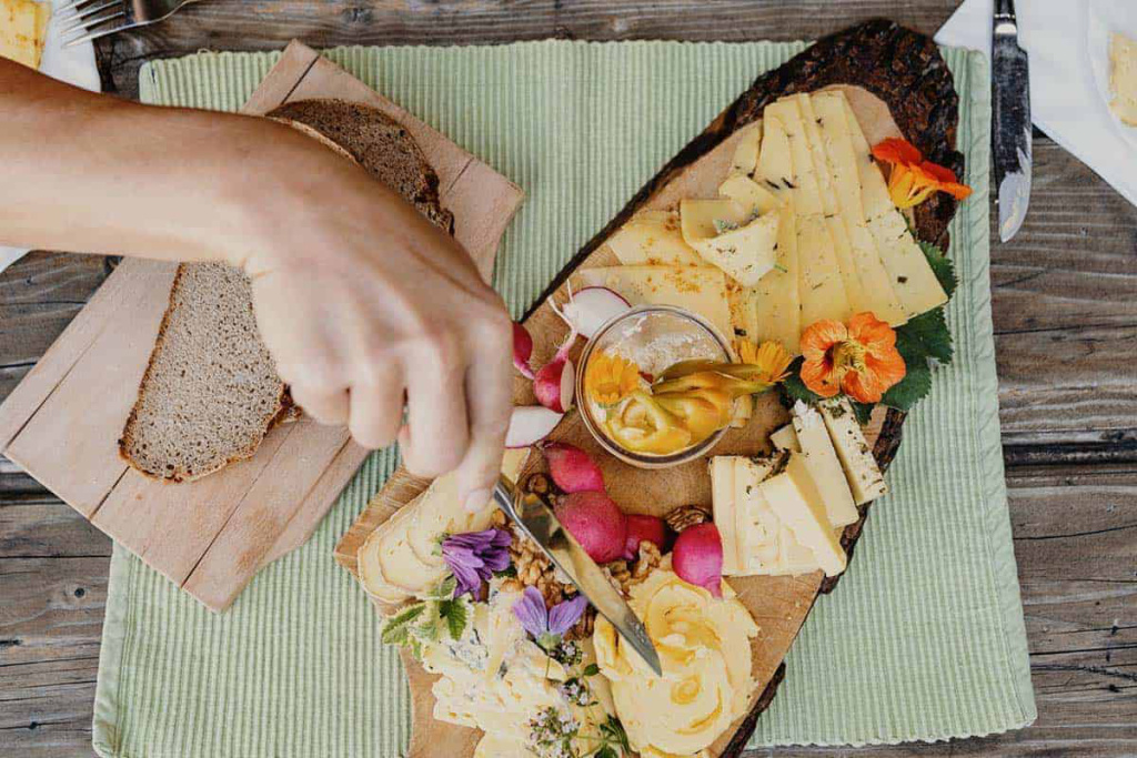 Bunte Käseplatte mit frischen Radieschen und Brot auf einem Holzteller.