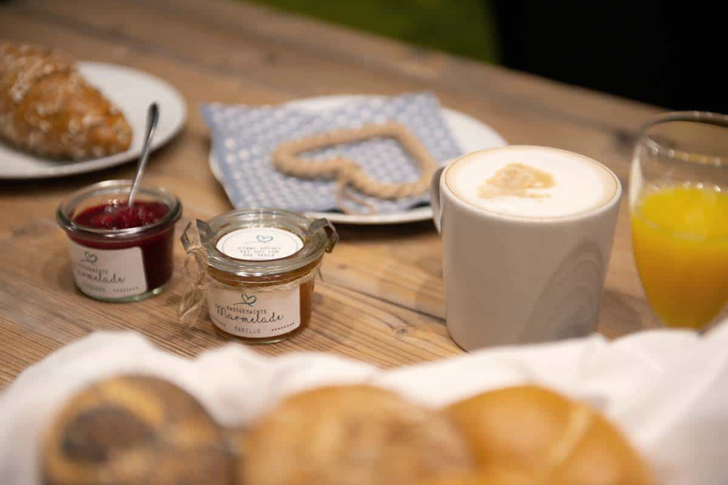 Frühstückstisch mit Croissant, Marmelade, Kaffee und Saft in gemütlicher Atmosphäre.