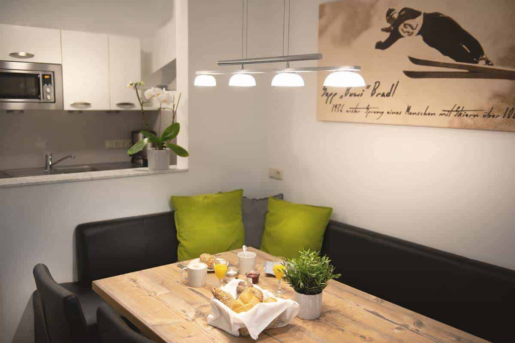 Gemütlicher Essbereich mit Frühstück, Küchenzeile und Skifahrer-Bild im Apartmenthaus Rainer.