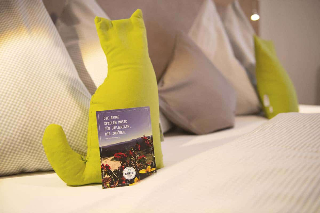 Grünes Kissen in Katzenform mit Karte auf Bett in Ferienwohnung in Mühlbach am Hochkönig.