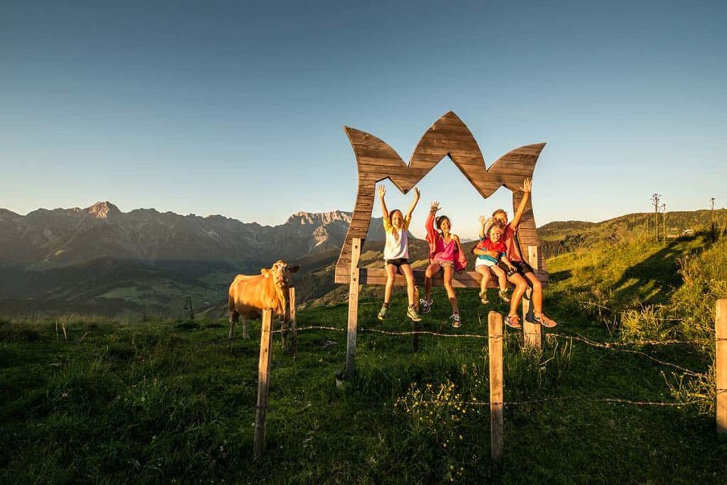Kinder sitzen glücklich auf einer Holzbank mit Bergblick in Mühlbach am Hochkönig.