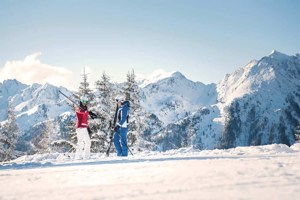 Paar im Schnee mit Skiausrüstung vor verschneiten Bergen in Mühlbach am Hochkönig.