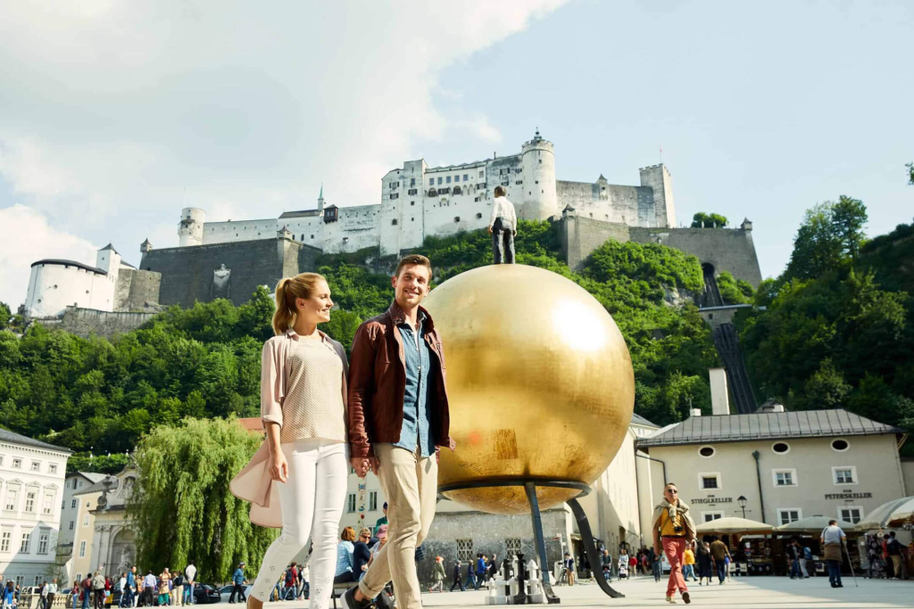 Paar spaziert vor goldener Kugel und Festung Hohensalzburg in Salzburg.
