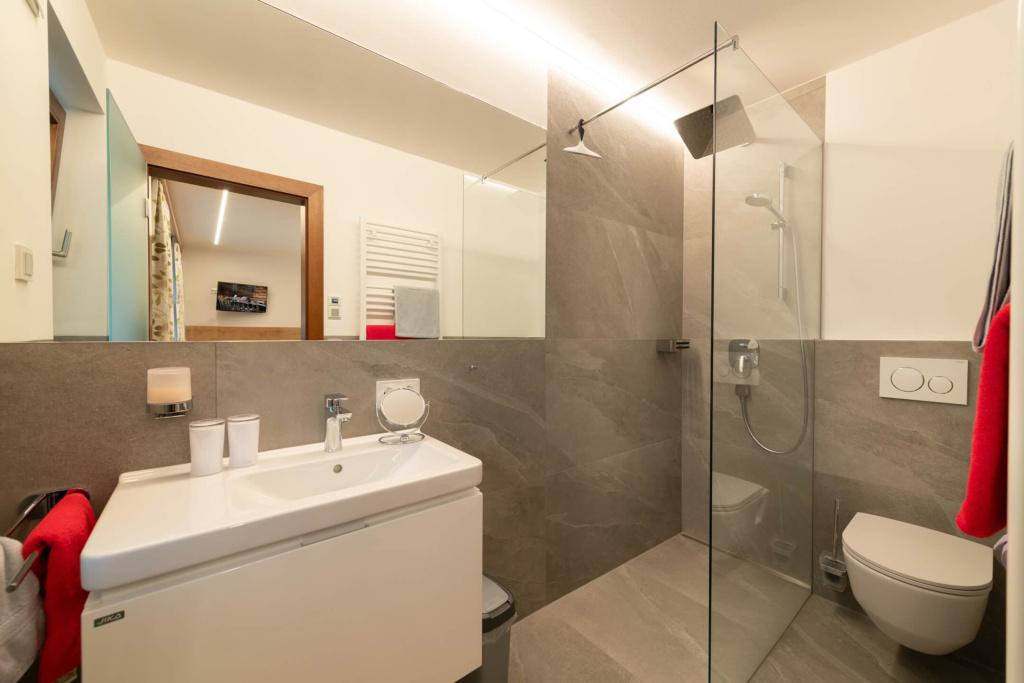 Modernes Badezimmer mit Dusche, Waschbecken und eleganter Fliesenoptik im Apartmenthaus Rainer.