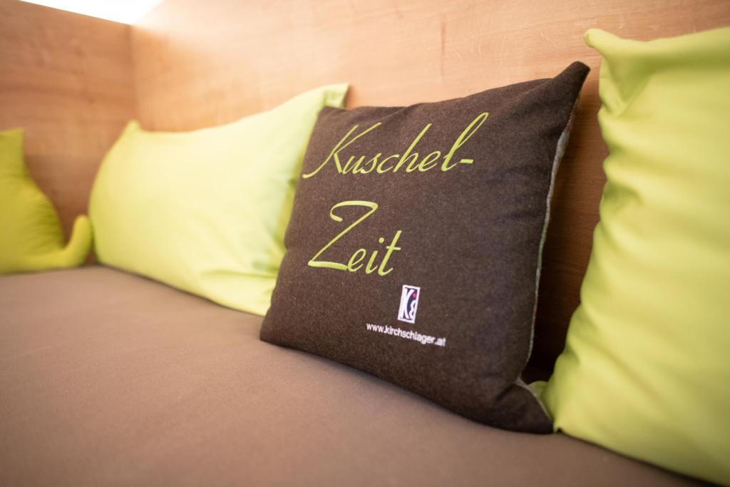Kissen mit der Aufschrift "Kuschel-Zeit" auf einer gemütlichen Bank in einem Apartment.